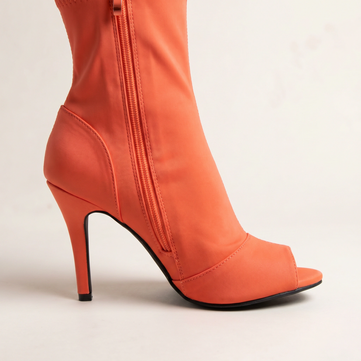 Orange high-heeled boot with a zipper on a light beige background