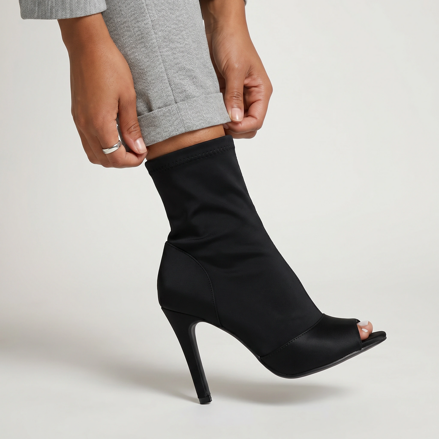 Black high-heeled sock boot being worn on a light gray background