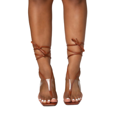 Amber clear strap heels with brown ankle ties worn on feet with white polished nails